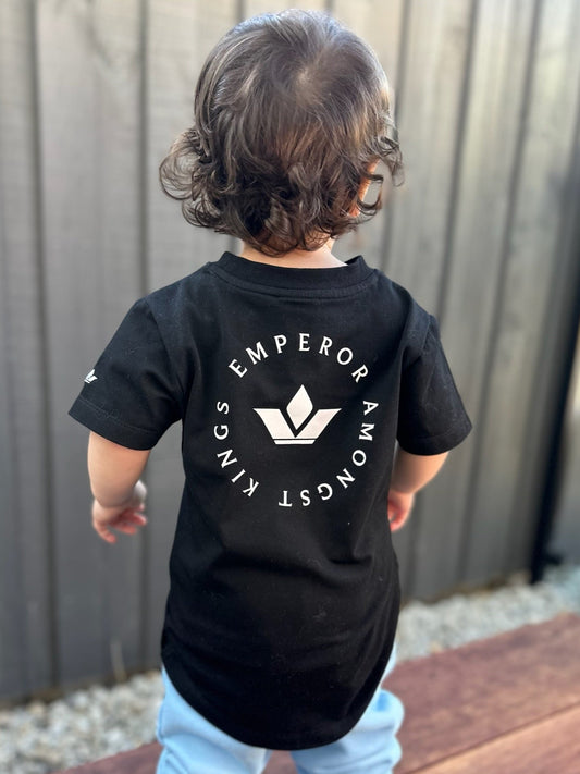 Child wearing a black t-shirt with a logo and text, standing outdoors.