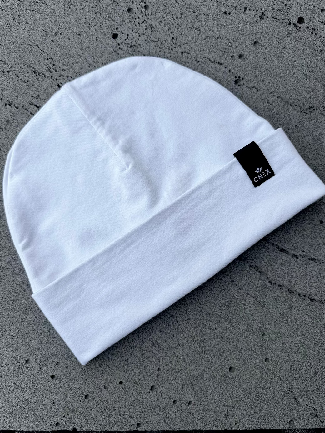 White beanie with a brand logo on a gray textured background