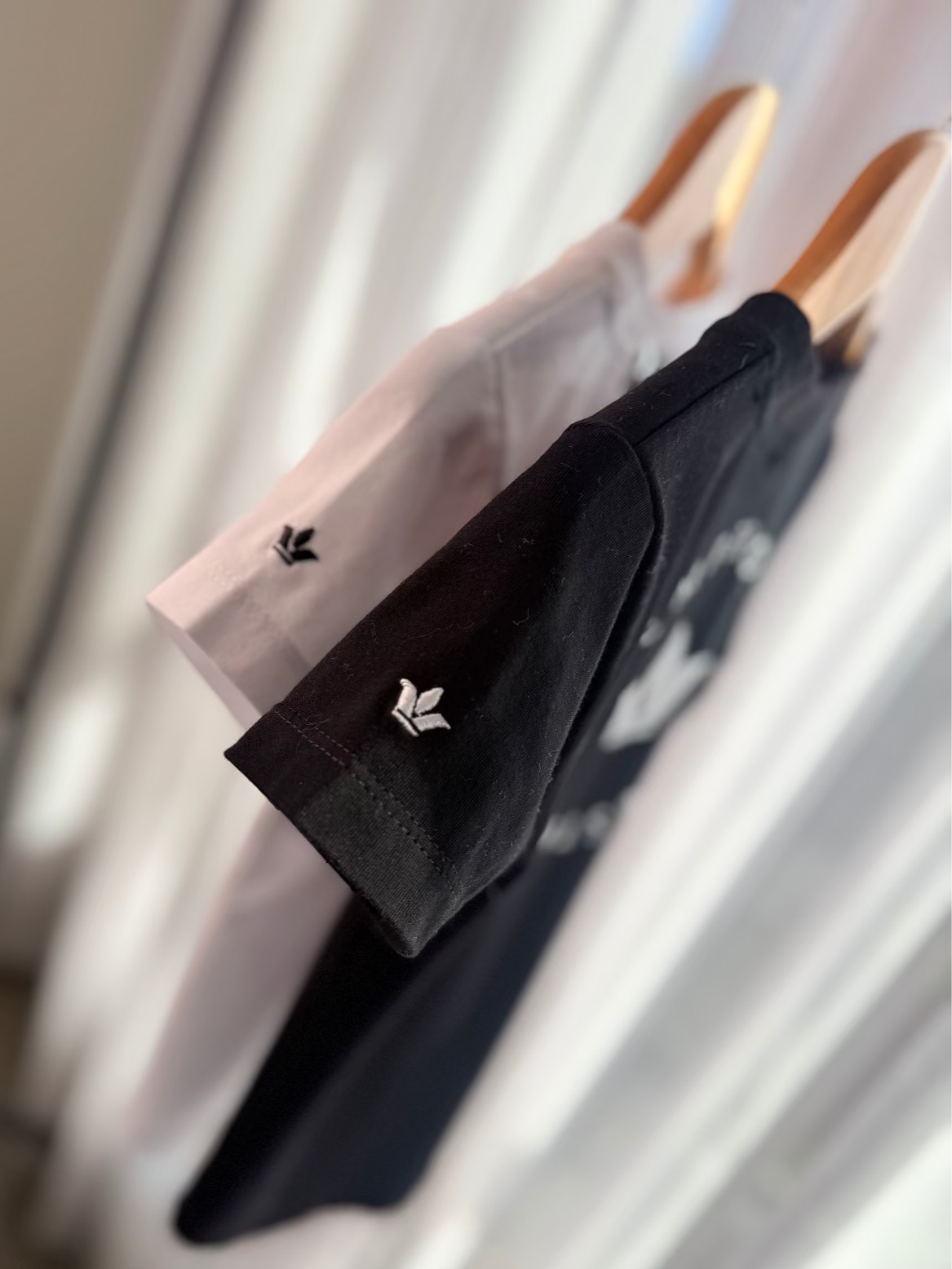 Two shirts, one black and one white, hanging on a rack with a blurred background.