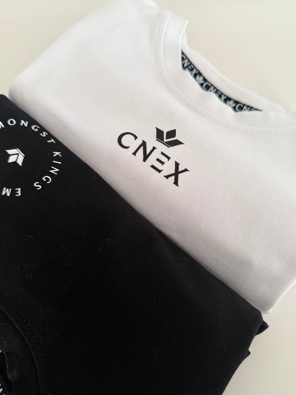 Two folded t-shirts, one black and one white, with 'CNEX' branding on a light background.
