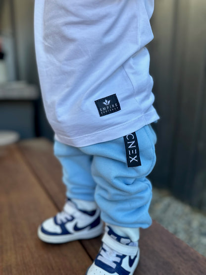 Child wearing light blue pants with visible brand labels, standing on a wooden floor.