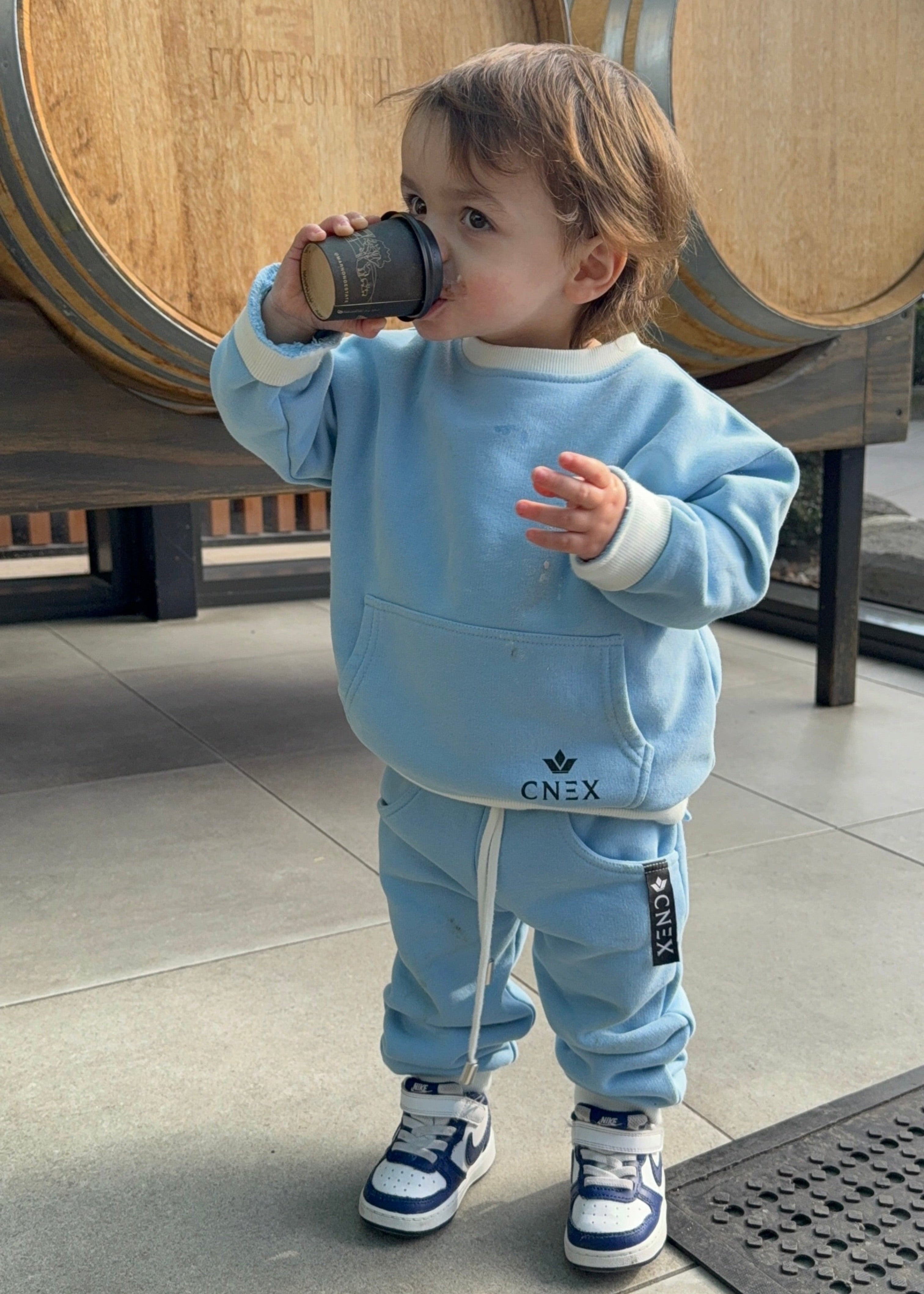 Child in a blue outfit standing next to wooden barrels
