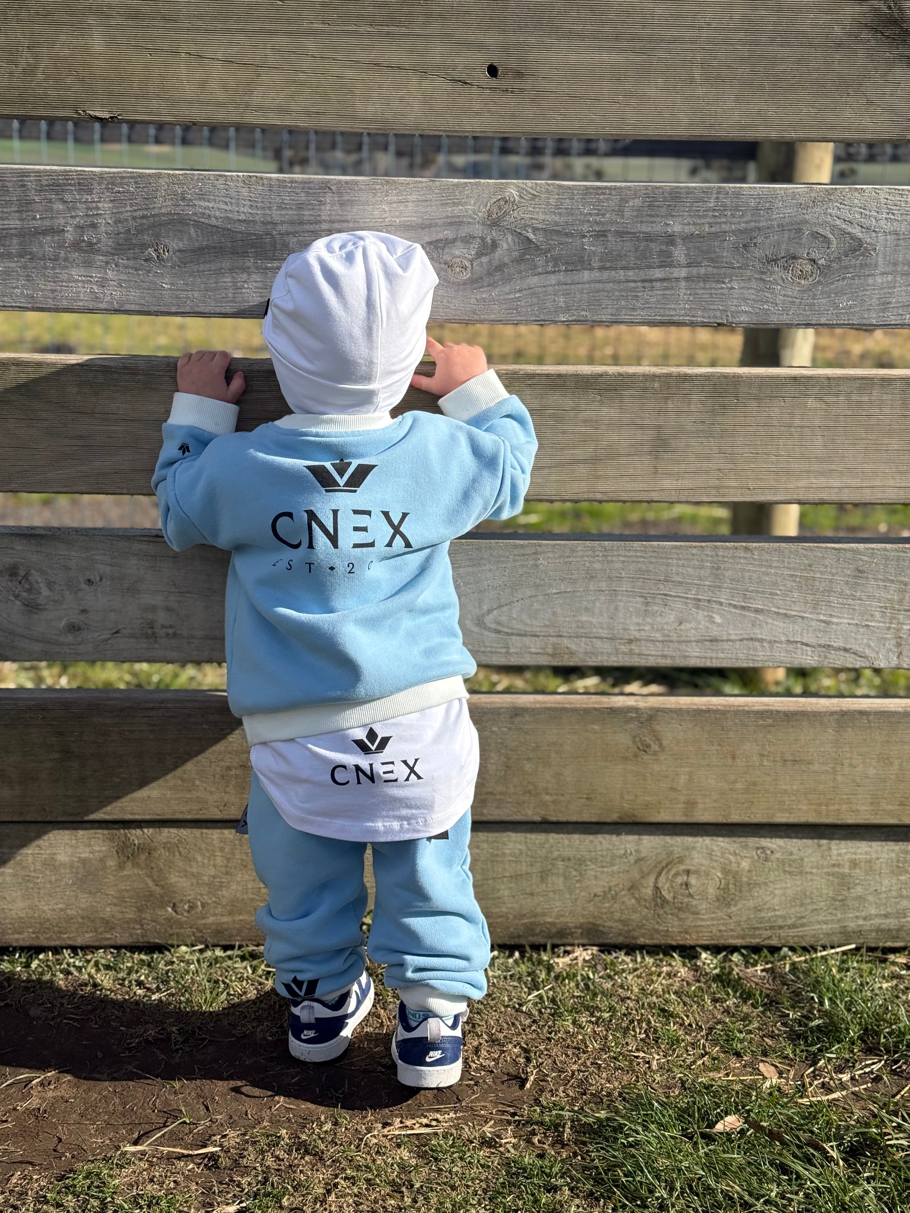 Child wearing a CNEX outfit standing against a wooden fence.