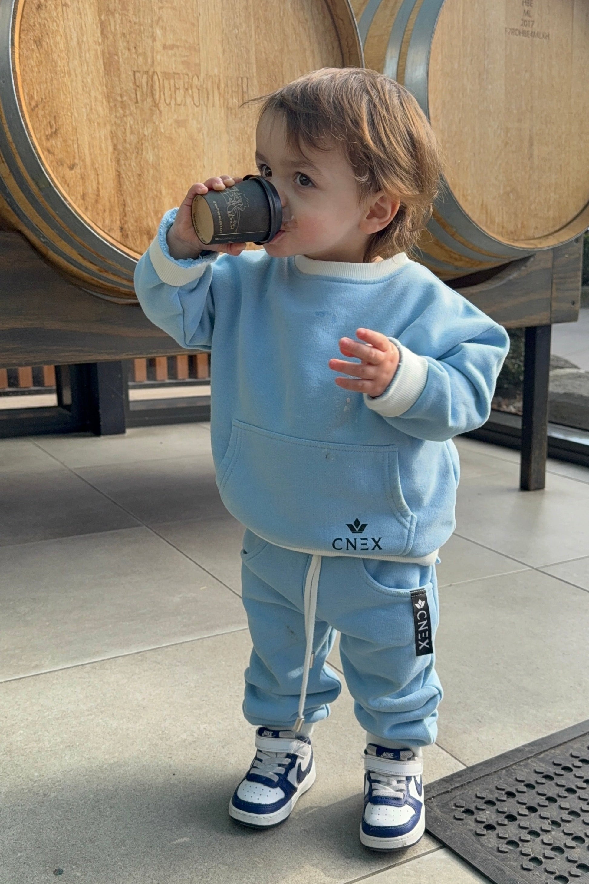 Child in a blue outfit standing next to wooden barrels